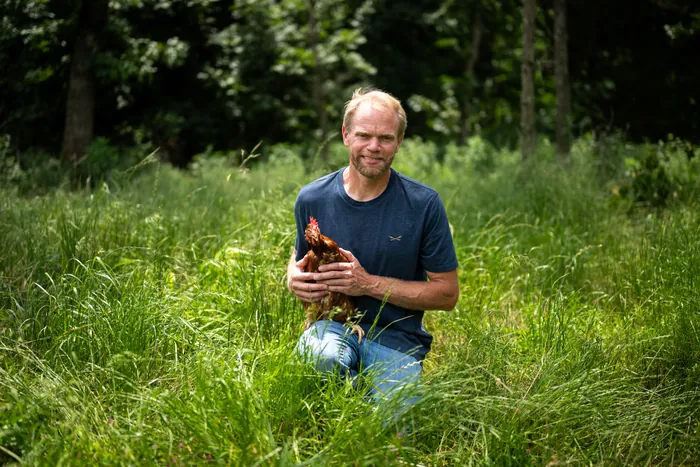 A farmer kneeling in tall grass, holding one of his hens