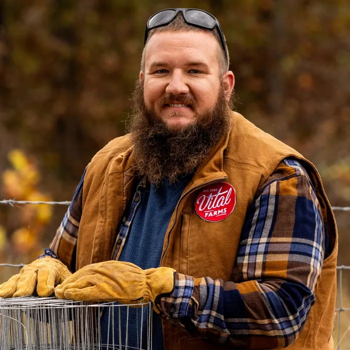 A bearded farmer in a canvas jacket, smiling towards the camera