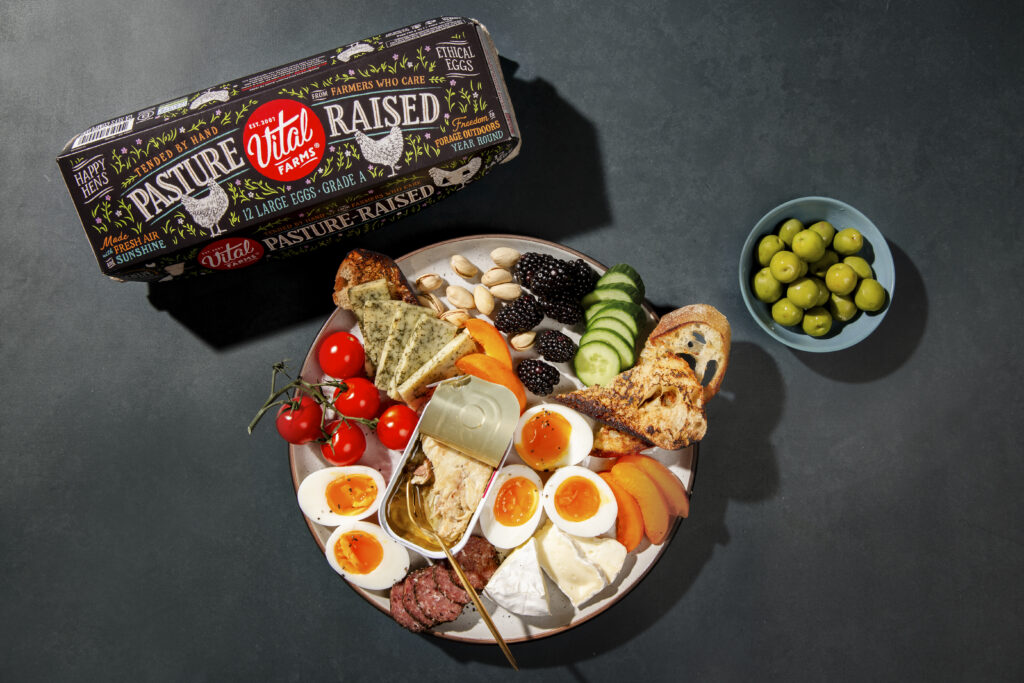 Charcuterie board with soft-boiled eggs, cheese, fruit, and fish beside a Vital Farms egg carton.