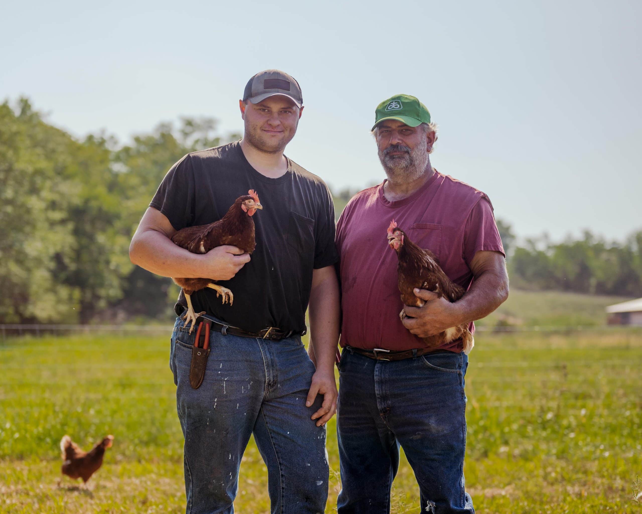two family farmers holding chickens on a pasture