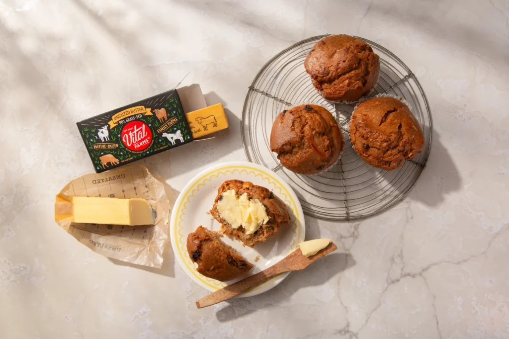 A plated muffin spread with butter and muffins on a cooling rack alongside a package of Vital Farms Pasture-Raised Butter.