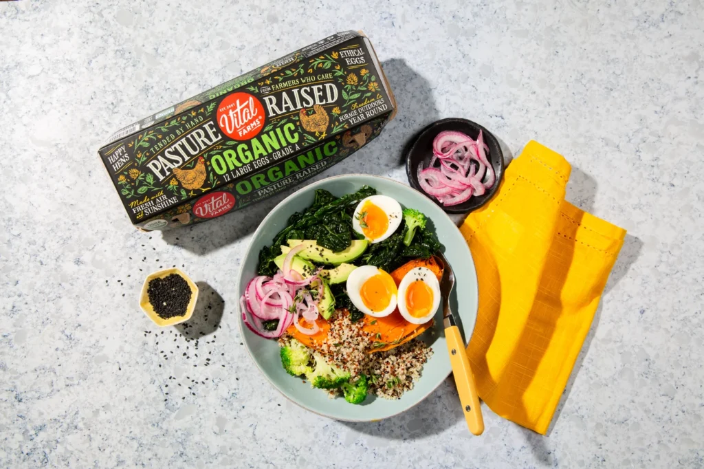 Power bowl with jammy eggs on counter with carton of Organic Pasture-Raised eggs and garnishes like pickled red onions and sesame seeds.